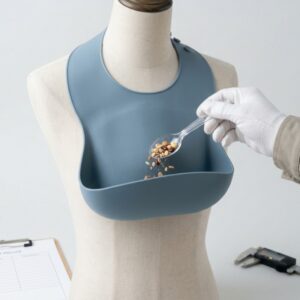 Silicone baby bib fitted to a torso display form during a food-catching pocket evaluation