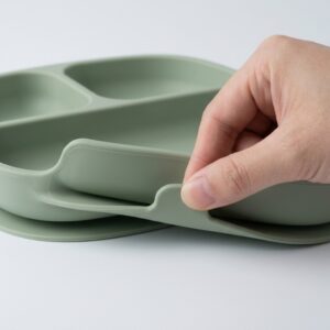 Adult hand evaluating the release tab on a three-compartment silicone baby suction plate